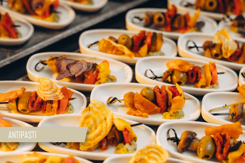 Skewered antipasti on small white plates with olives, peppers, and grilled vegetables, arranged for serving.