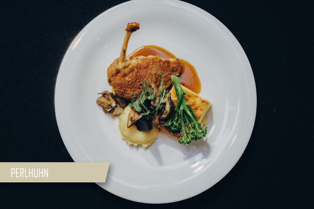 Plate with crispy roasted chicken leg, mashed potatoes, sautéed mushrooms, and greens with brown sauce on a white plate against a dark surface.